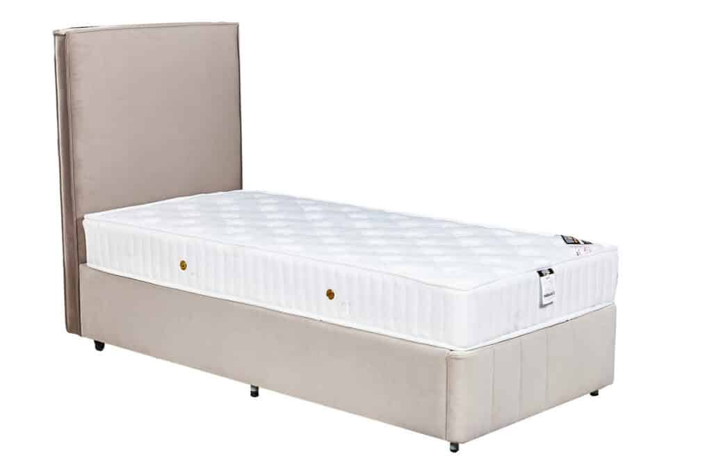 מיטה יחיד בצבע בז' עם ראש מיטה מרופד ומזרן לבן.