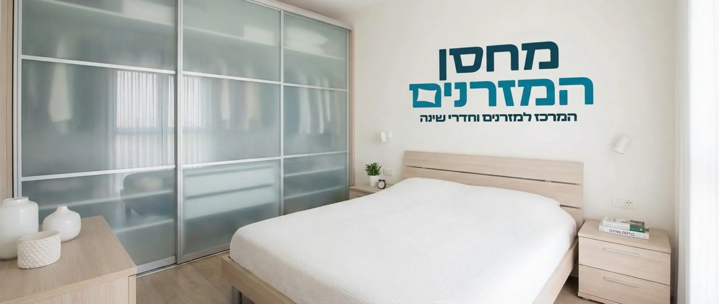 חדר שינה זוגי מואר עם ארון הזזה גדול בעל דלתות זכוכית חלבית אטומה, שידות צד תואמות מעץ בהיר בקו נקי ומינימליסטי. חלל מסודר המשדר שלווה ארגונית מופתית. אין אנשים בתמונה.